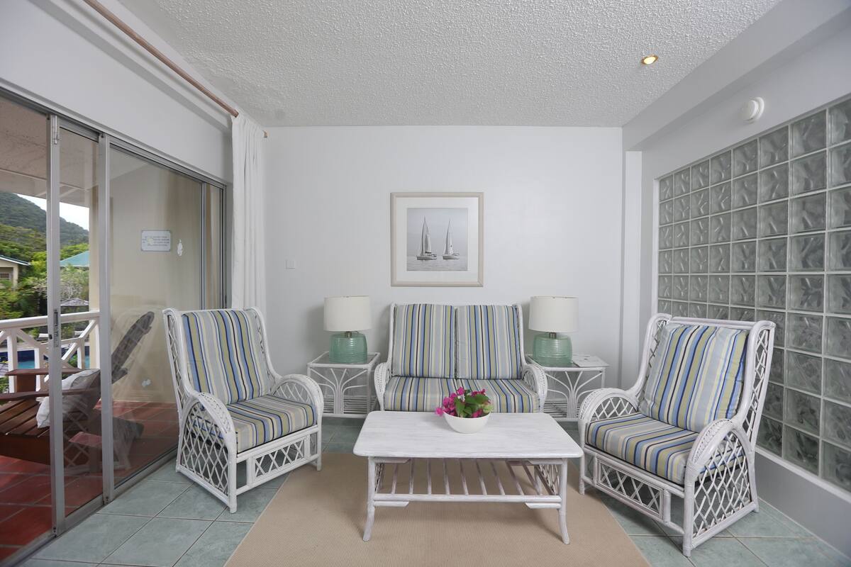 A balcony with wicker chairs, a white table, and a framed picture of sailboats.