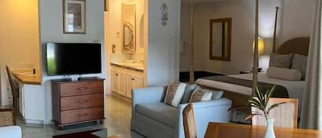 A living room with a sofa, a coffee table, a TV, and a dining table with chairs.