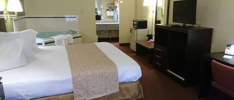 Una habitación de hotel con una cama grande, un escritorio con computadora, un televisor y un espejo.