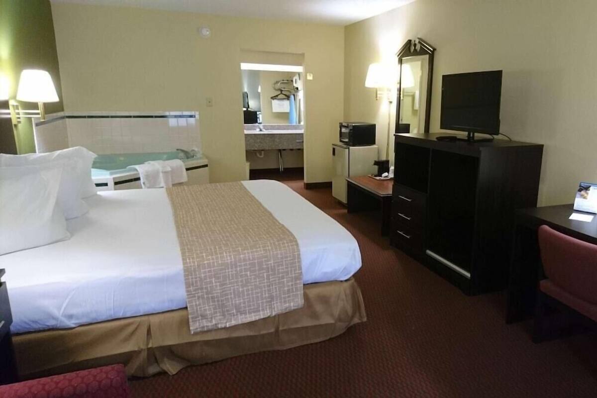 Et hotelværelse med en stor seng, et skrivebord med en computer, et fjernsyn og et spejl.