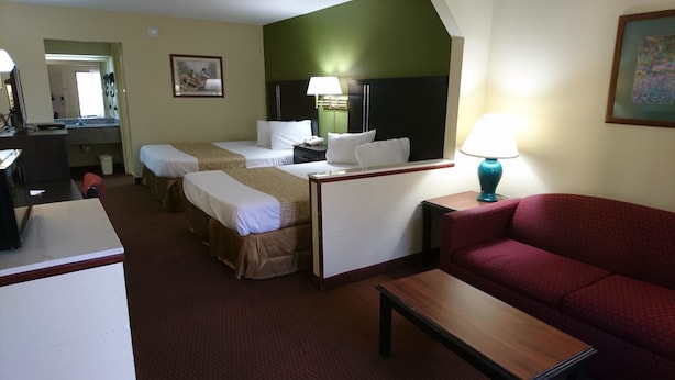 Quarto de hotel com duas camas de solteiro, uma escrivaninha, um sofá vermelho e uma televisão.