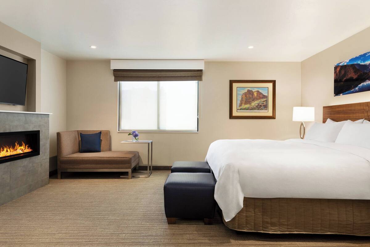 Quarto de hotel com uma cama, um sofá, uma mesinha, uma televisão, lareira e janela com vista.