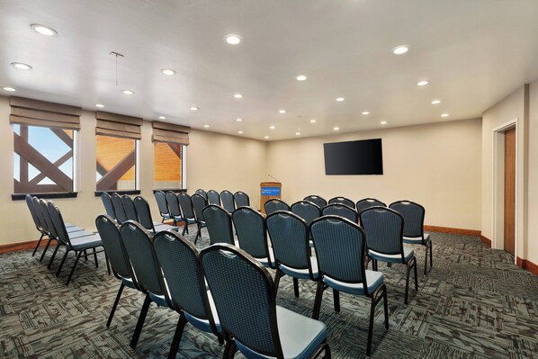 A conference room with rows of chairs, a podium, and a large screen on the wall.