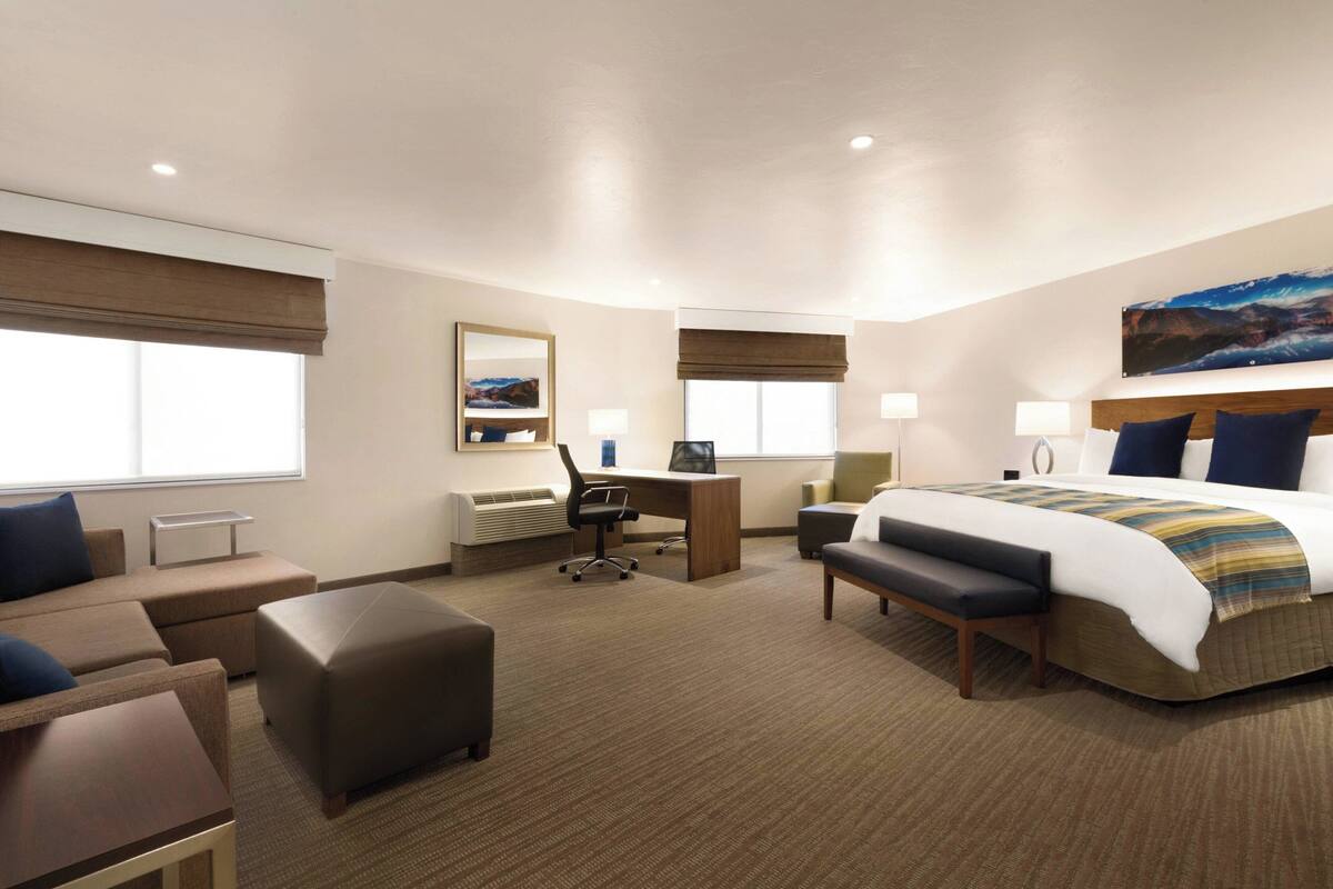 Quarto de hotel com cama, escrivaninha, cadeira, sofá e mesa pequena.