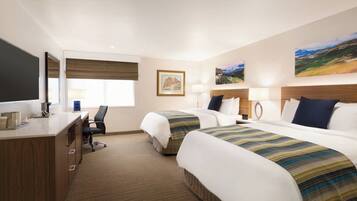 A hotel room with two beds, a desk, a chair, and a large window with blinds.