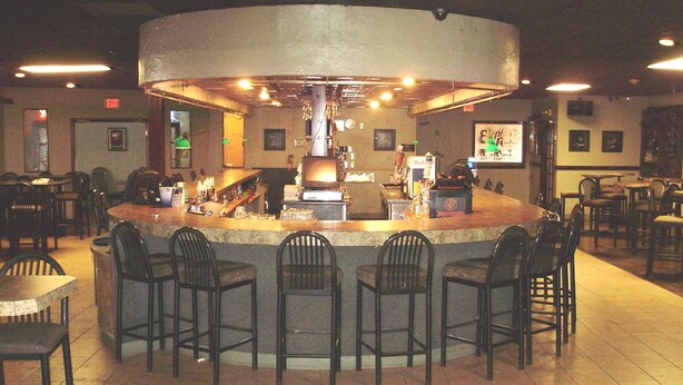 A bar area with a central counter, multiple bar stools, and a tiled floor. - Trade Winds Central Inn (Tulsa)