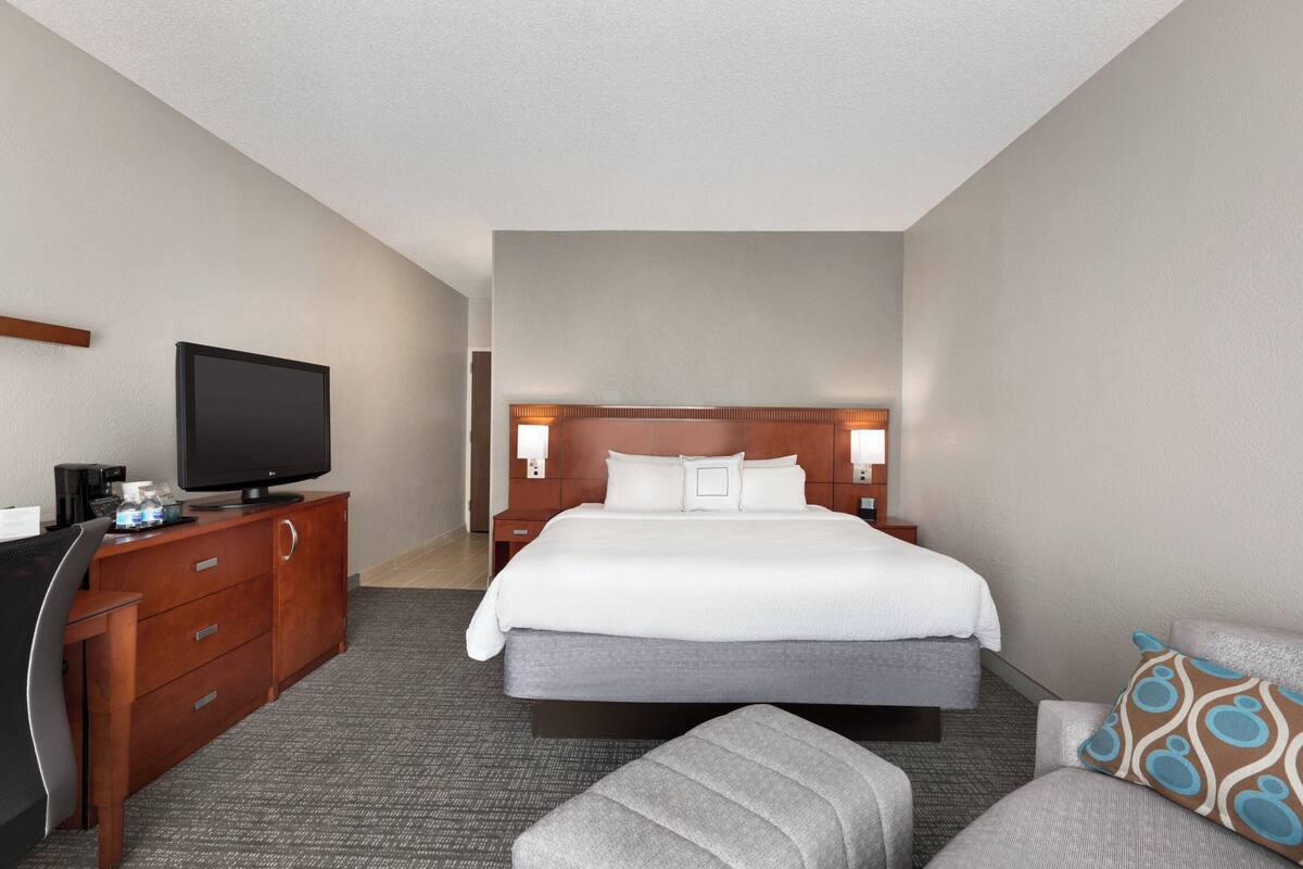 Ein Hotelzimmer mit Bett, Schreibtisch mit Fernseher, Stuhl und Sofa.