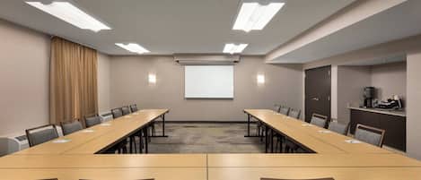 A conference room with a long table, chairs, a projector screen, and a coffee machine.