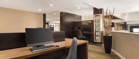 A modern reception desk with a computer, a keyboard, and a chair. There is a sign that reads "Boarding Pass" and a bookshelf with books and decorative items.