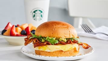Um sanduíche de café da manhã em um prato, com uma xícara da Starbucks ao fundo.