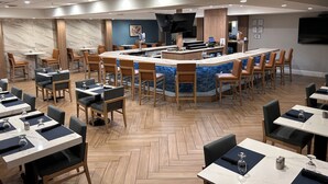 A modern hotel lobby with a central bar, dining tables, and bar stools.