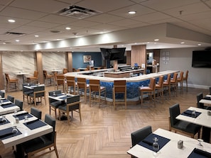 Un hall d’hôtel moderne avec un bar central, des tables à manger et des tabourets de bar.