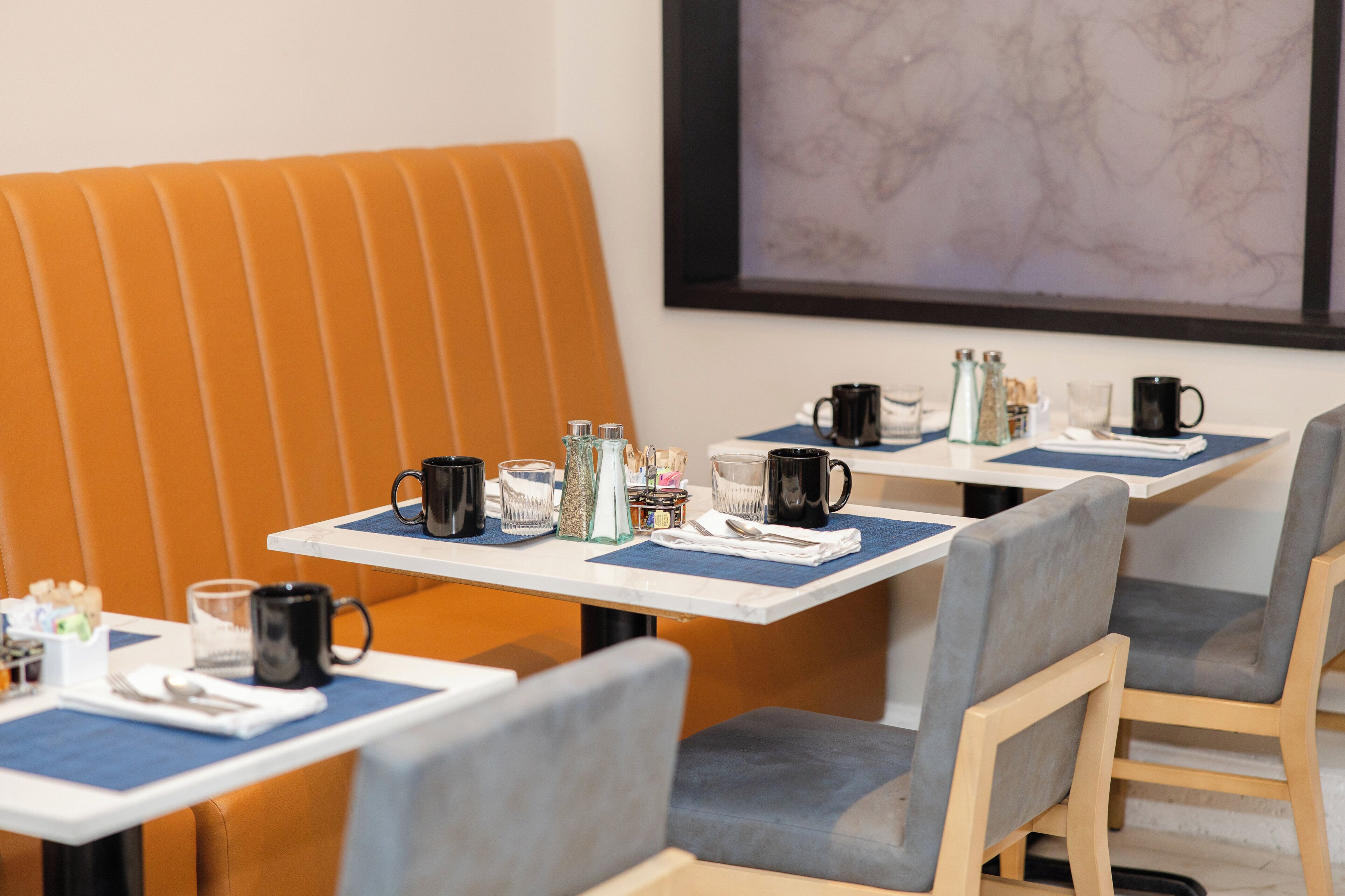 Un espace repas aménagé avec des banquettes et des tables, chacune étant équipée d’un assortiment de tasses, de verres et de condiments.