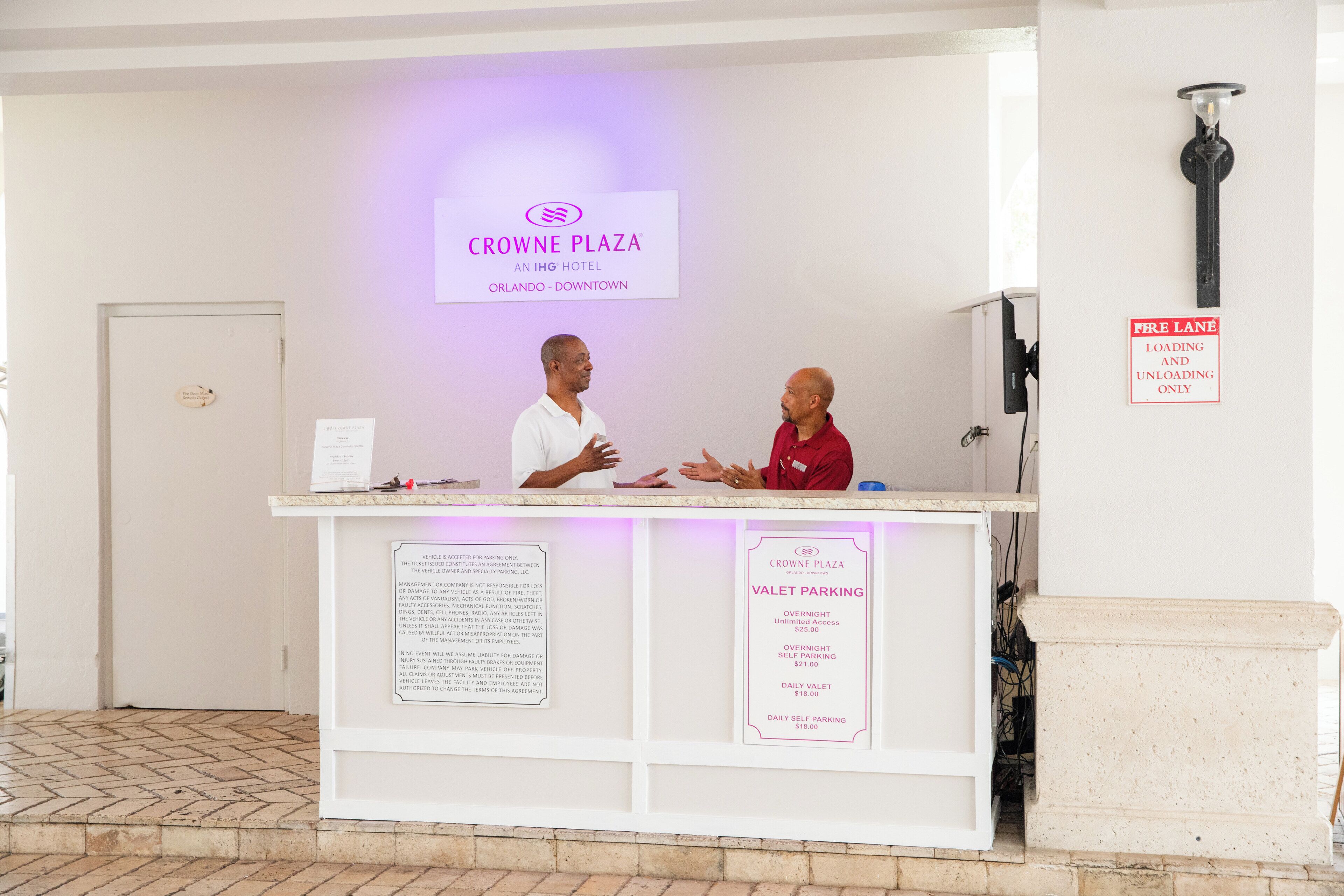 Una receptione d'albergo con la segnaletica Crowne Plaza, un hotel IHG, e informazioni sul servizio di parcheggio con conducente.