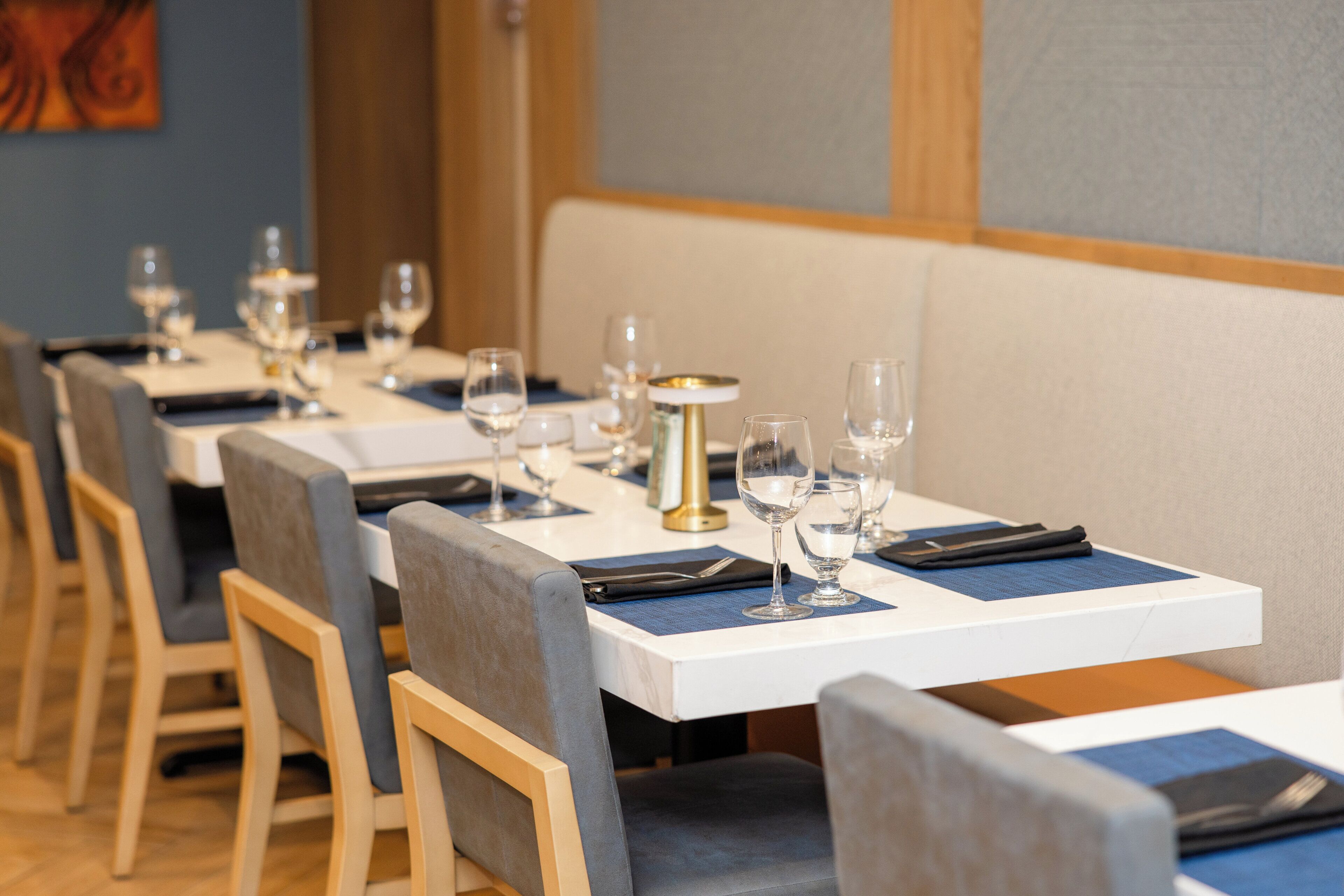 A row of dining tables with chairs, each table set with wine glasses and napkins.