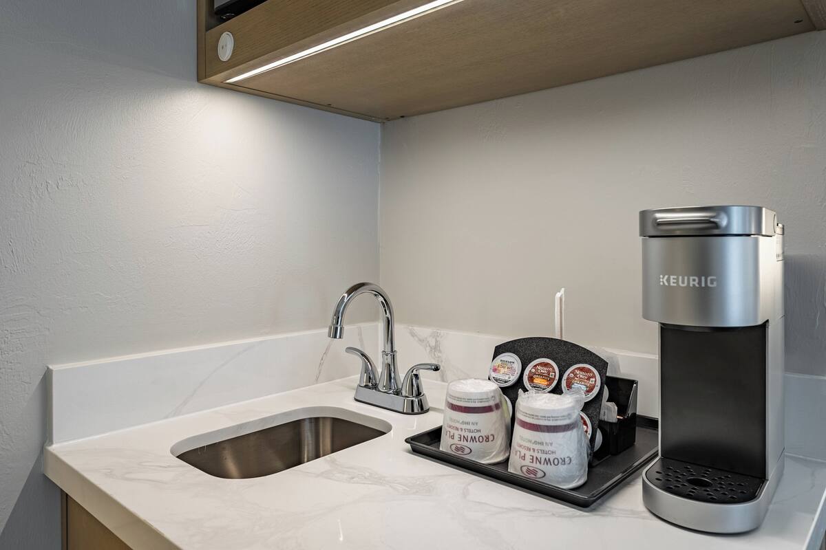Une petite cuisine équipée d’une machine à café Keurig, d’un évier et de deux dosettes de café présentées sur un plateau.
