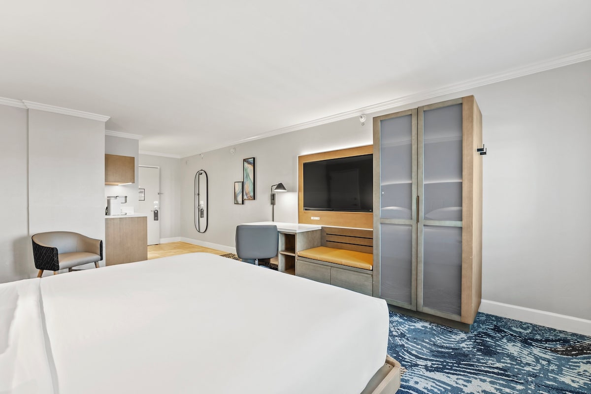 Una habitación de hotel con una cama grande, un escritorio con una silla, un televisor y un armario.
