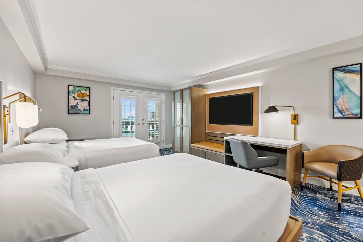 Une chambre d’hôtel avec deux lits, un bureau, une chaise, une télévision et une fenêtre donnant sur un paysage agréable.