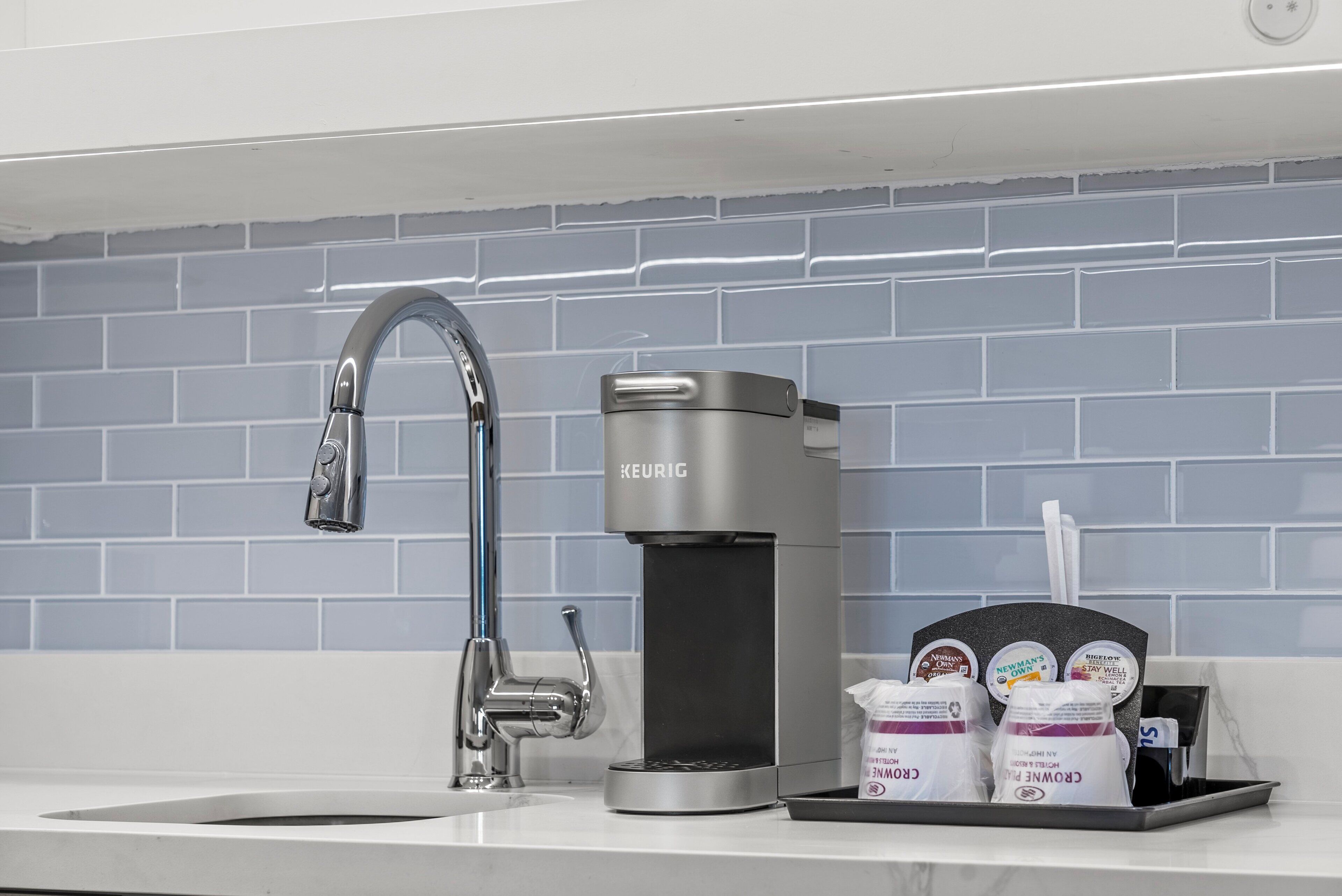 Una cocina moderna con una elegante cafetera de acero inoxidable, un lavamanos individual y una bandeja con cápsulas de café.