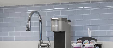 Una cocina moderna con una elegante cafetera de acero inoxidable, un lavamanos individual y una bandeja con cápsulas de café.