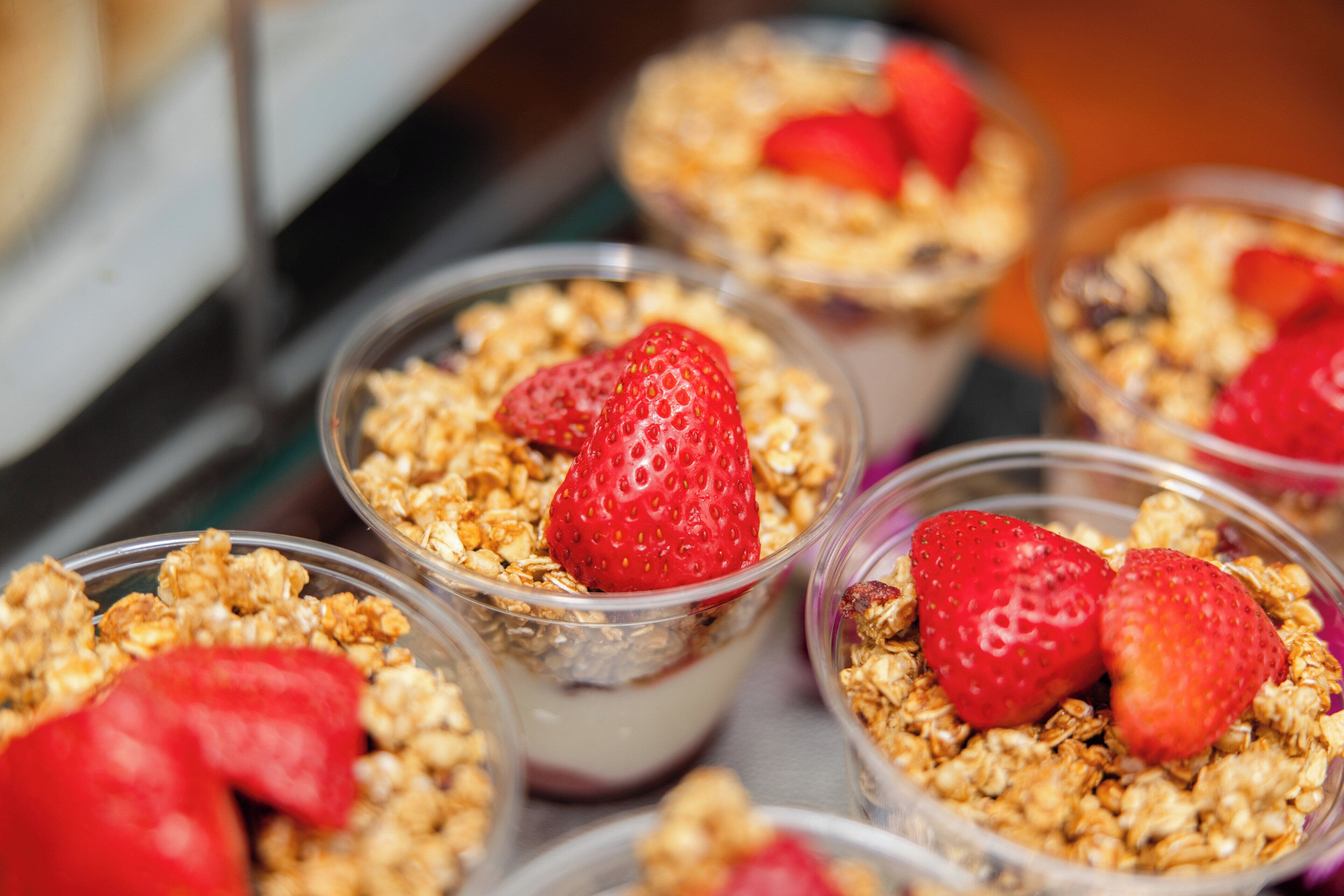 A close-up of several clear plastic cups filled with granola and strawberries.