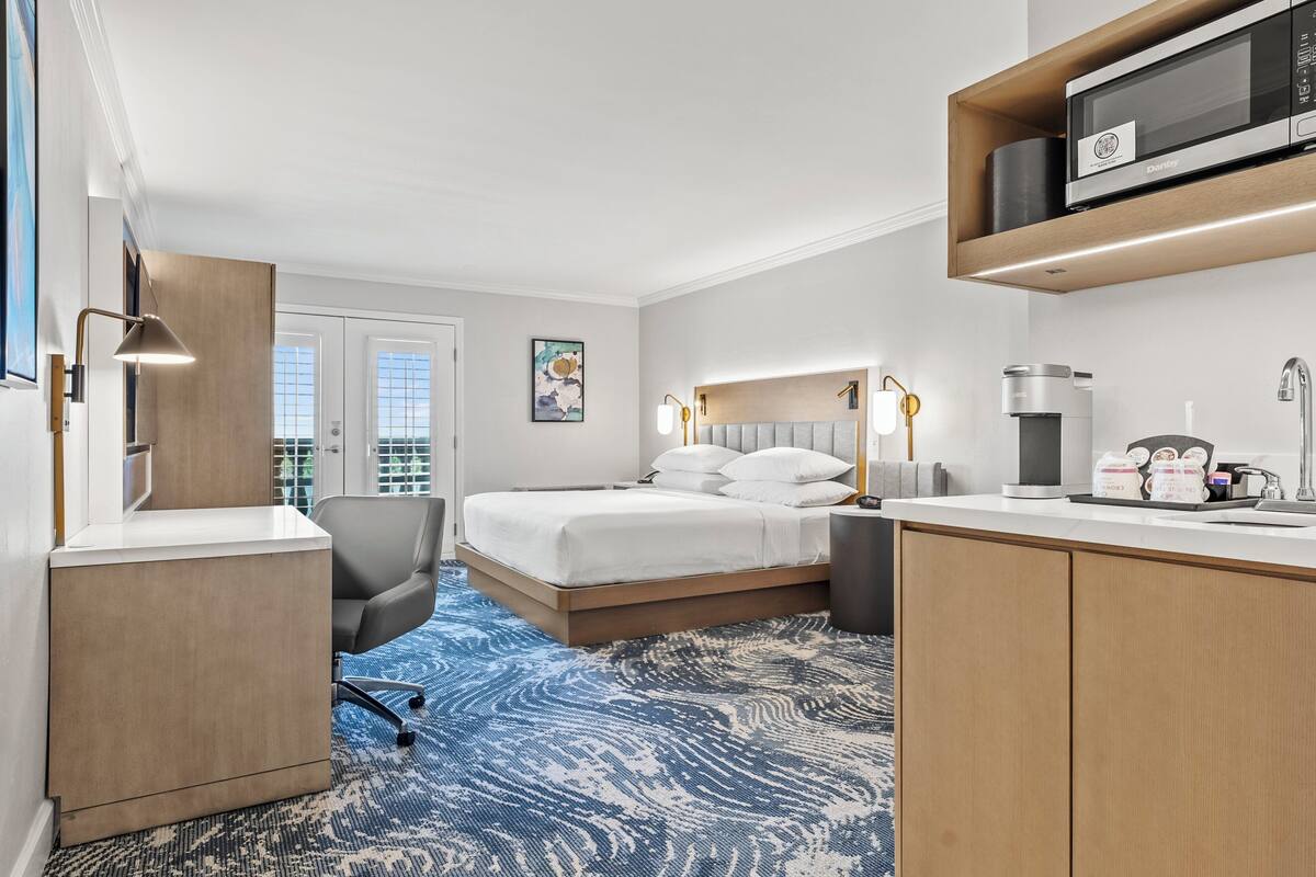 Une chambre d’hôtel équipée d’un lit, d’un bureau, d’une chaise et d’un four à micro-ondes posé sur le comptoir.