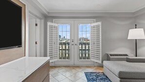 Een moderne woonkamer met een grote flatscreen televisie, een grijze bank, een vloerkleed met blauw patroon en een witte vloerlamp.