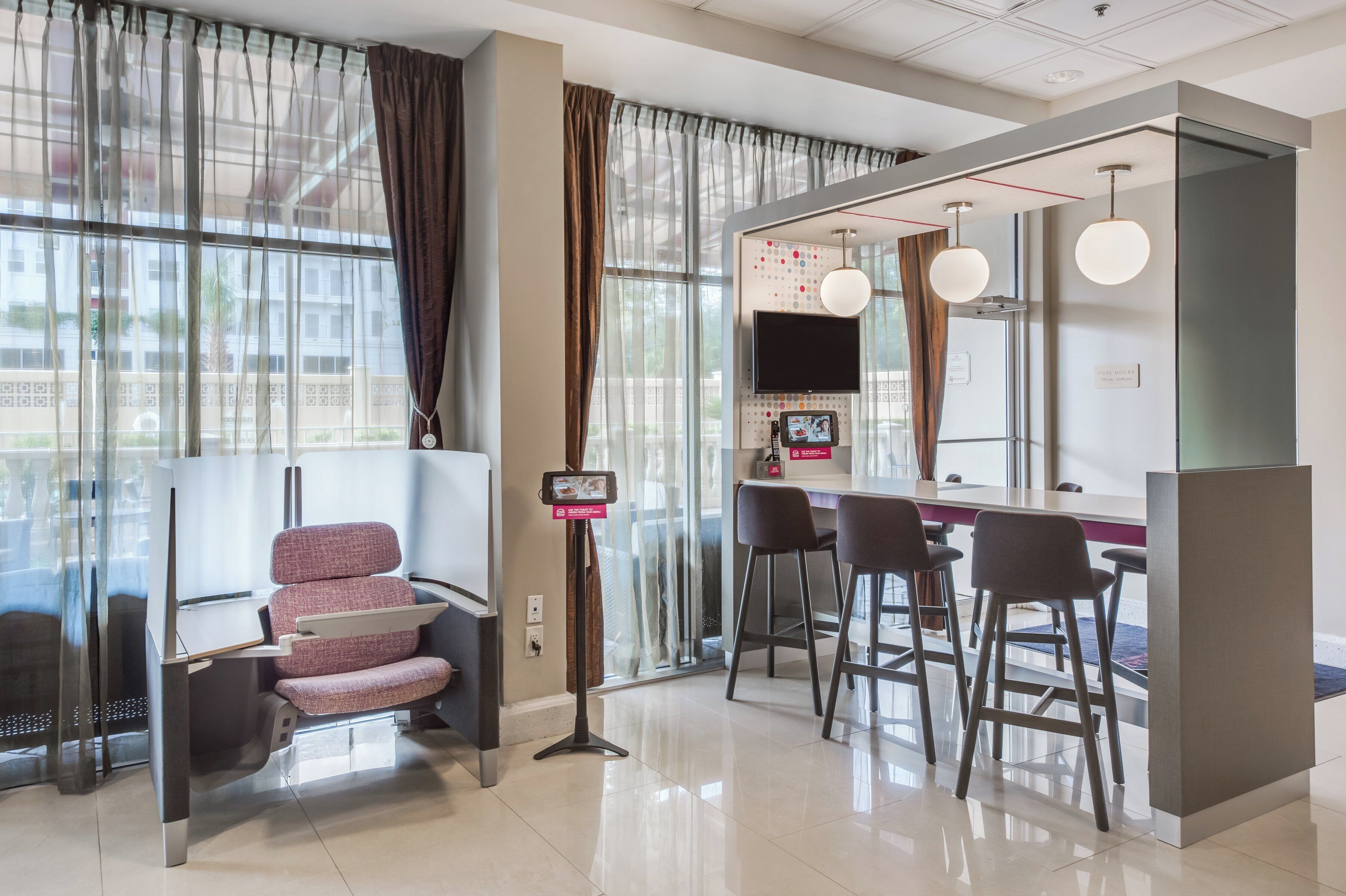 A modern hotel room with a seating area, a television, and a digital menu board.