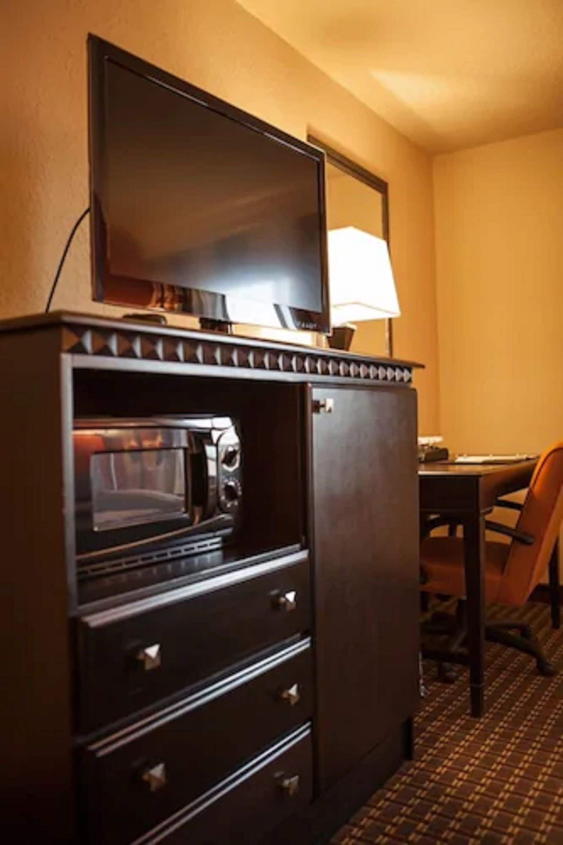 A compact kitchenette with a microwave, oven, and a flat-screen TV on top.