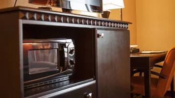 A compact kitchenette with a microwave, oven, and a flat-screen TV on top.