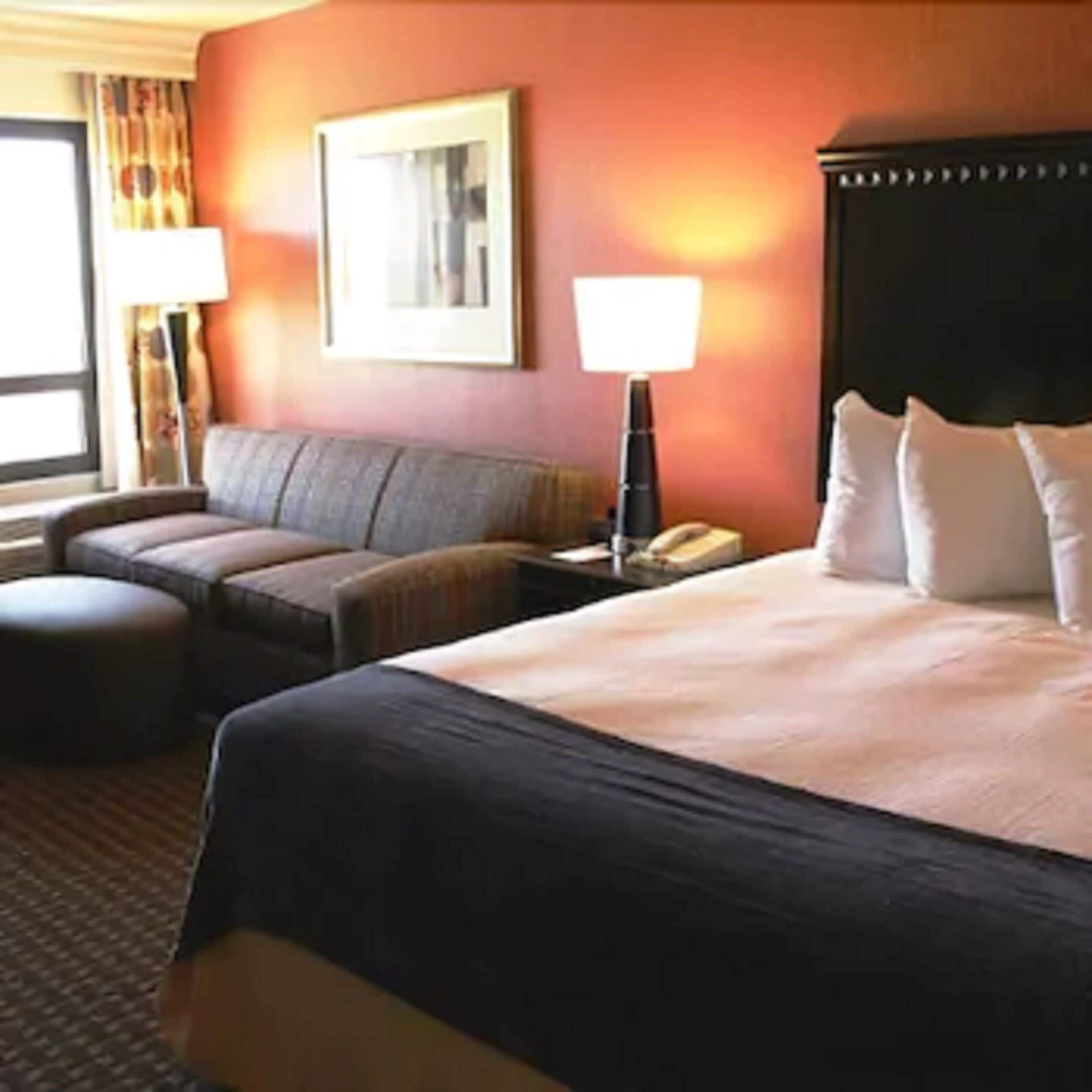 Una habitación de hotel con una cama grande, un sofá, una mesita y una lámpara.