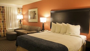 A hotel room with a large bed, a sofa, a chair, a lamp, and a painting on the wall. - Decatur Conference Center & Hotel (Decatur)