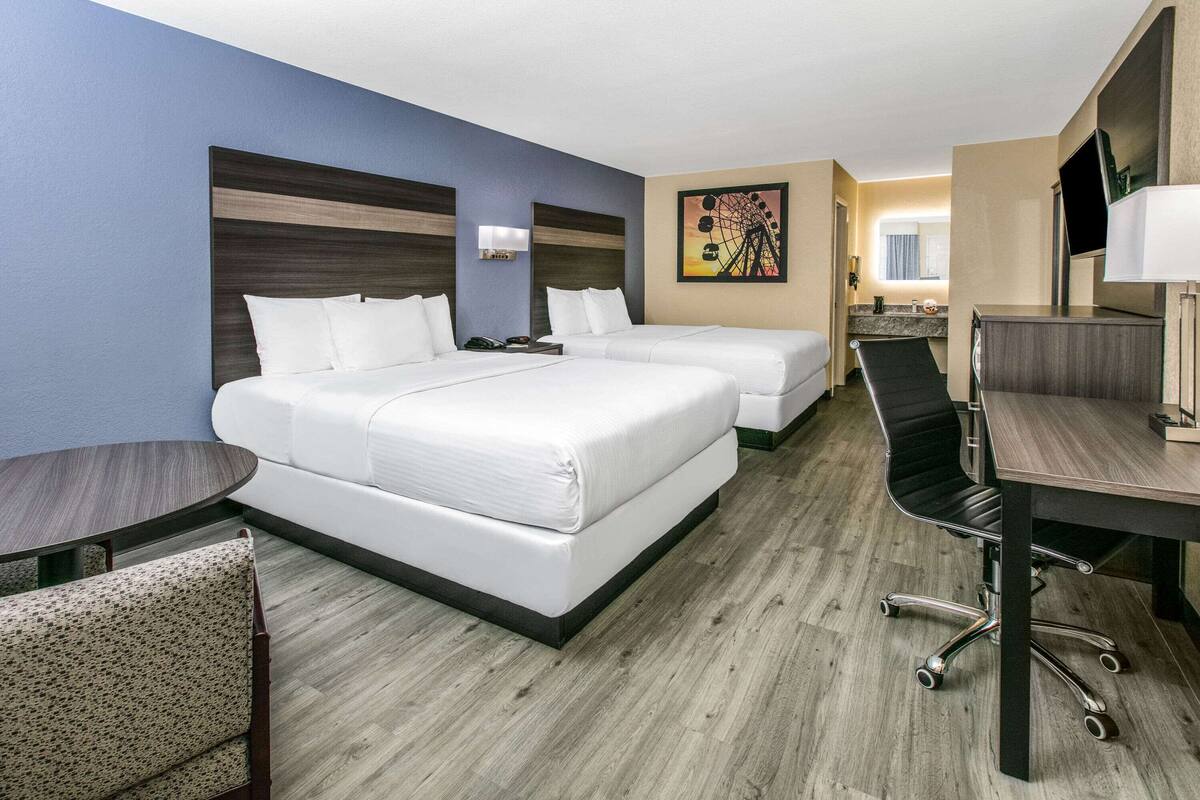 A hotel room with two beds, a desk, a chair, and a TV.