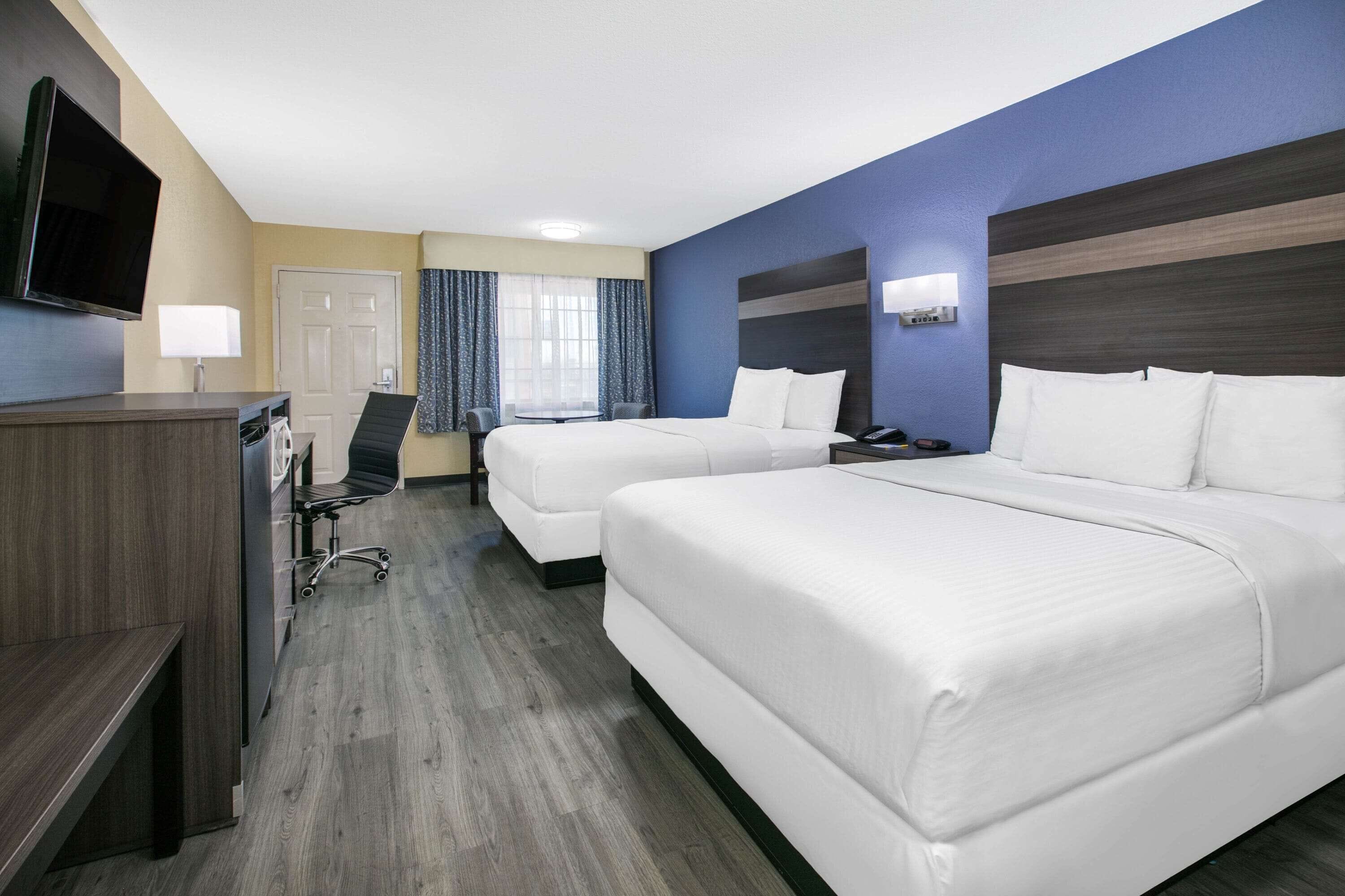 A hotel room with two beds, a desk with a chair, a television, and a window with curtains.