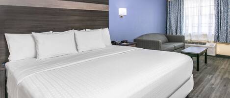 A hotel room with a large bed, a chair, a small table, and a window with curtains.