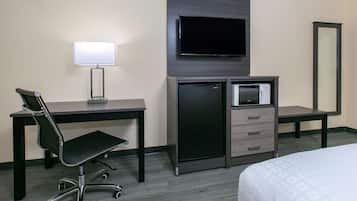 A hotel room with a desk, chair, TV, mini-fridge, and a bed.
