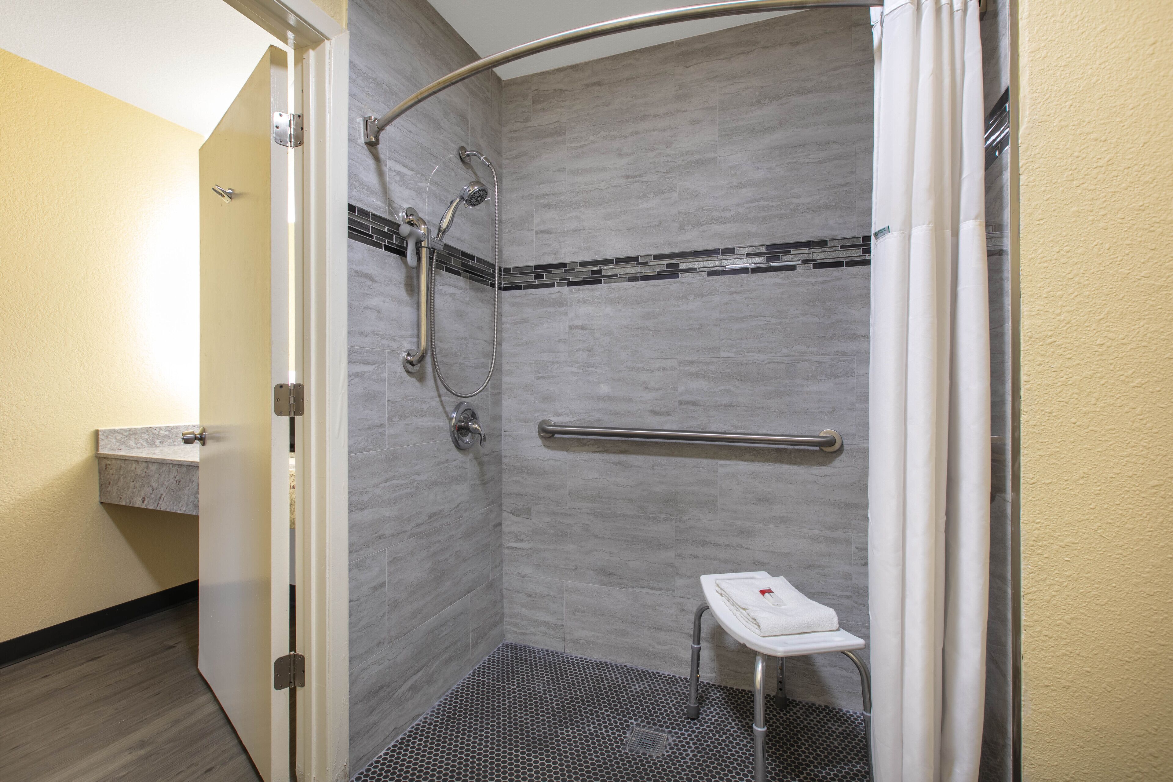 A walk-in shower with a handrail, a small stool, and a towel rack.