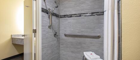 A walk-in shower with a handrail, a small stool, and a towel rack.