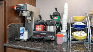 A kitchen area with a coffee machine, a coffee creamer dispenser, a Folgers coffee maker, and stacked paper cups.