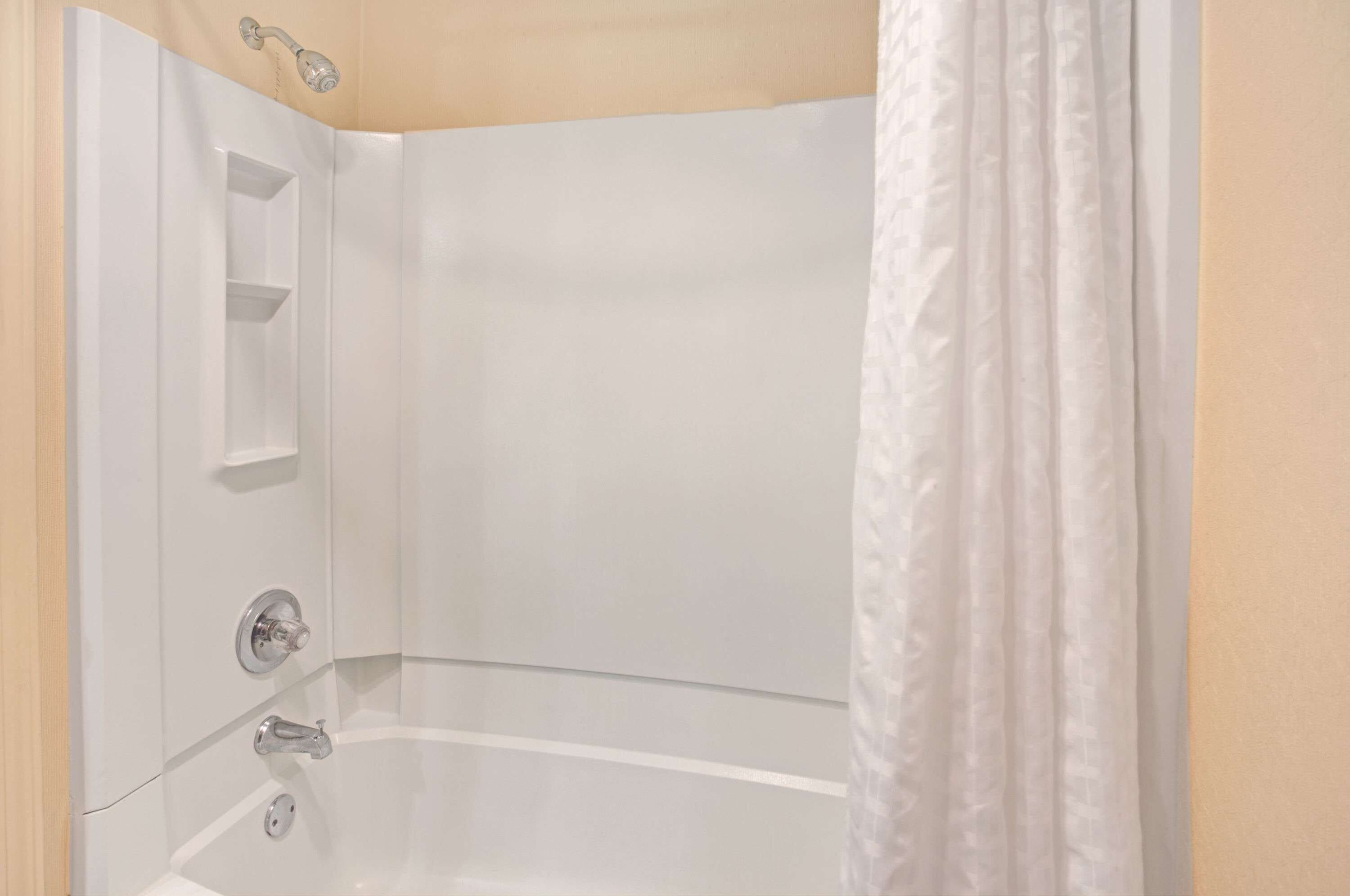 A corner of a bathroom with a white bathtub, a showerhead, and a white curtain.