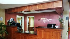 Een receptiebalie met een houten afwerking, een Dell computer en een bord met daarop Baymont Inn & Suites.
