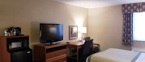 A hotel room with a television, desk, chair, two beds, and a window with curtains.