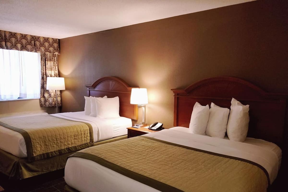 Une chambre d’hôtel avec deux lits, une table de chevet avec une lampe et une fenêtre avec des rideaux.