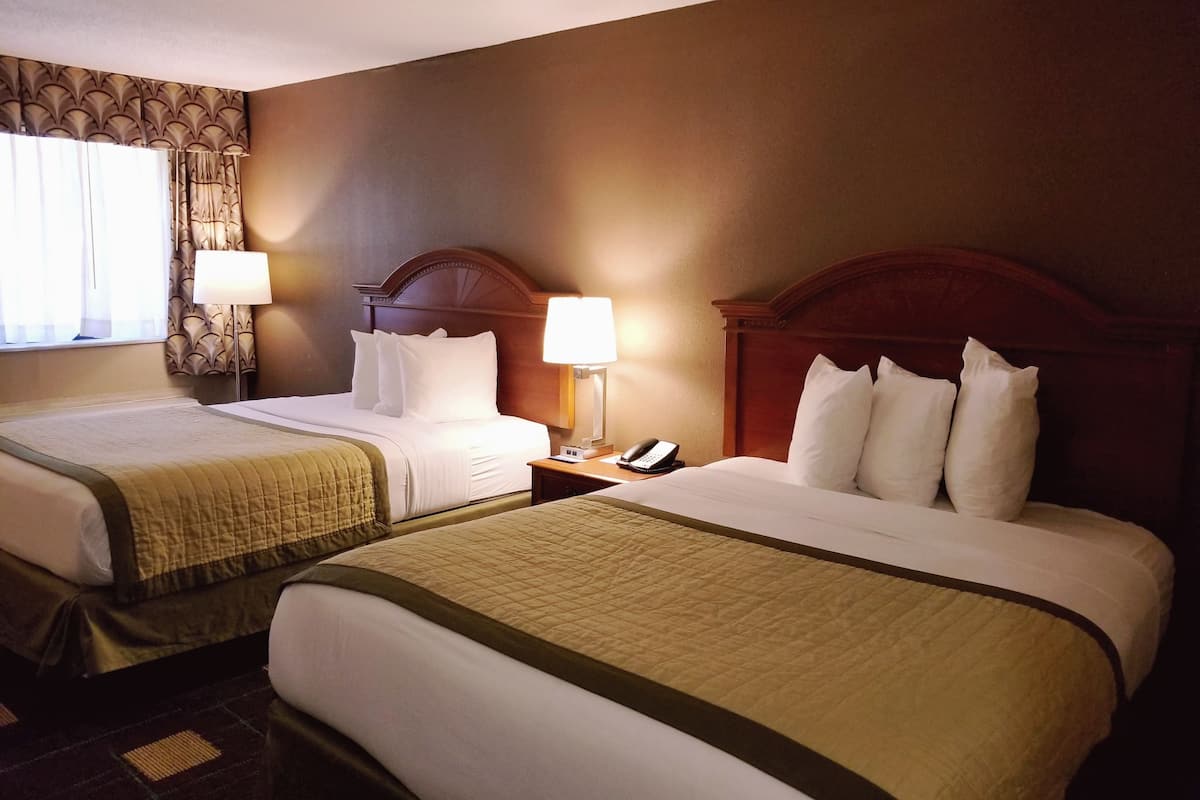 Une chambre d’hôtel avec deux lits, chacun doté d’une tête de lit en bois, de draps blancs et d’une couvre-lit matelassée. Une table de chevet avec une lampe et un téléphone se trouve sur le côté droit.