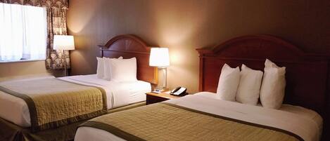 Quarto de hotel com duas camas, cada uma com cabeceira de madeira, roupa de cama branca e colcha acolchoada. Há uma mesa de cabeceira com uma luminária e um telefone ao lado direito.