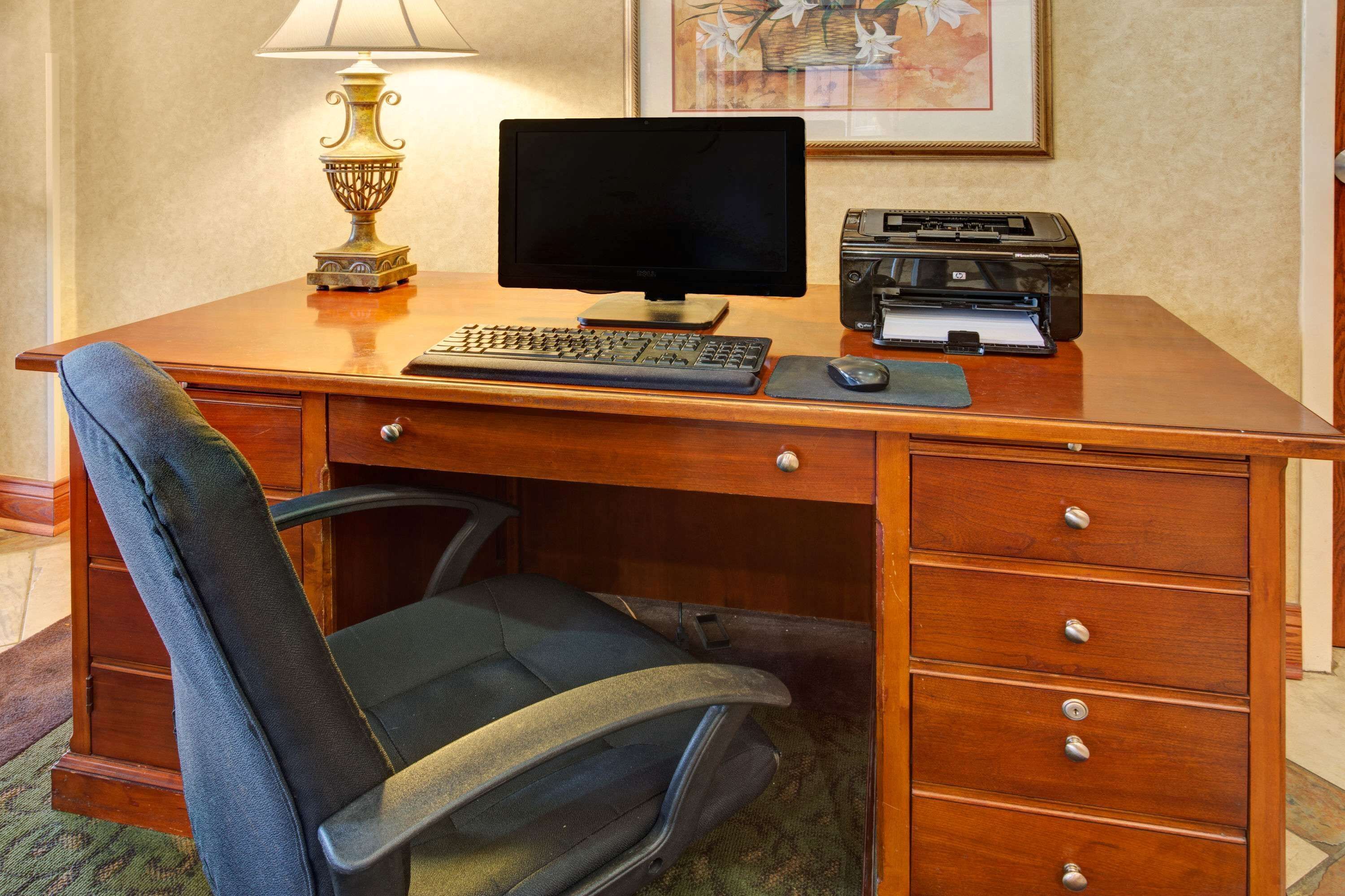 A wooden desk with a computer, keyboard, mouse, and printer. There is a chair in front of the desk.