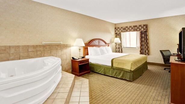 Hotelkamer met een groot bad, een bed met een groene dekbedovertrek, een nachtkastje met een lamp en een bureau met een televisie.
