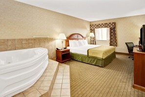Ein Hotelzimmer mit einer großen Badewanne, einem Bett mit einer grünen Tagesdecke, einem Nachttisch mit einer Lampe und einem Schreibtisch mit einem Fernseher.