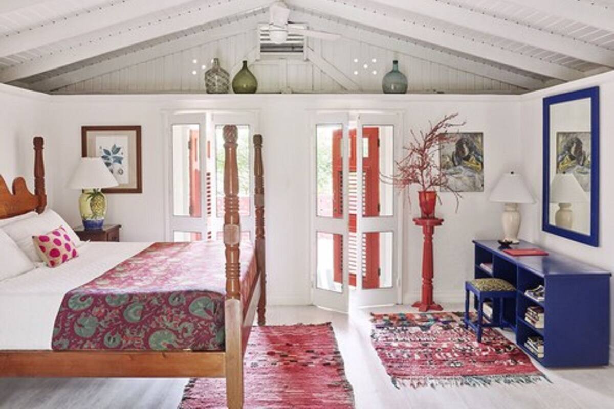 A bedroom with a wooden bed, a red and white striped door, a blue bookshelf, and a red vase.