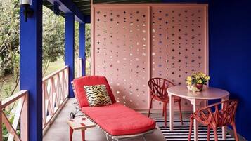 Un balcón con una silla lounge roja, una mesita con un jarrón de flores y una alfombra a rayas.